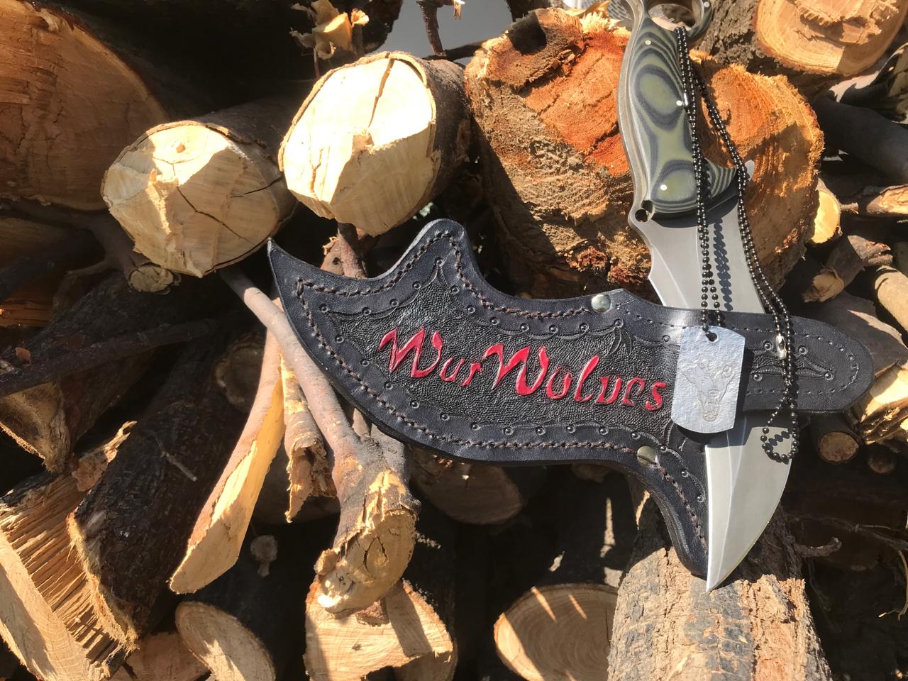 Commemorative War Wolves blade with its embroidered leather sheath and an original wolf tag, resting on stacked logs